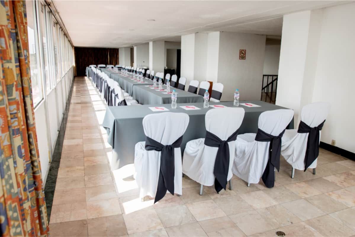 Un largo pasillo con mesas y sillas preparadas para una reunión.