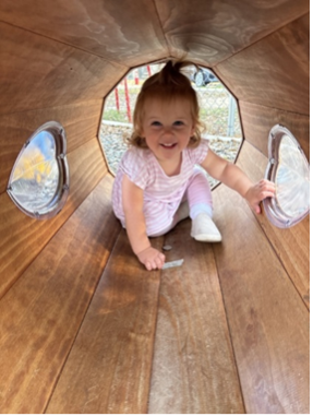 Smiling toddler crawls through wooden tunnel at playground.