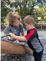 Two young children playing on playground equipment outdoors.