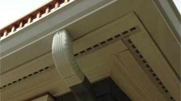 Corner of a building with a white gutter and downspout, and tan trim.