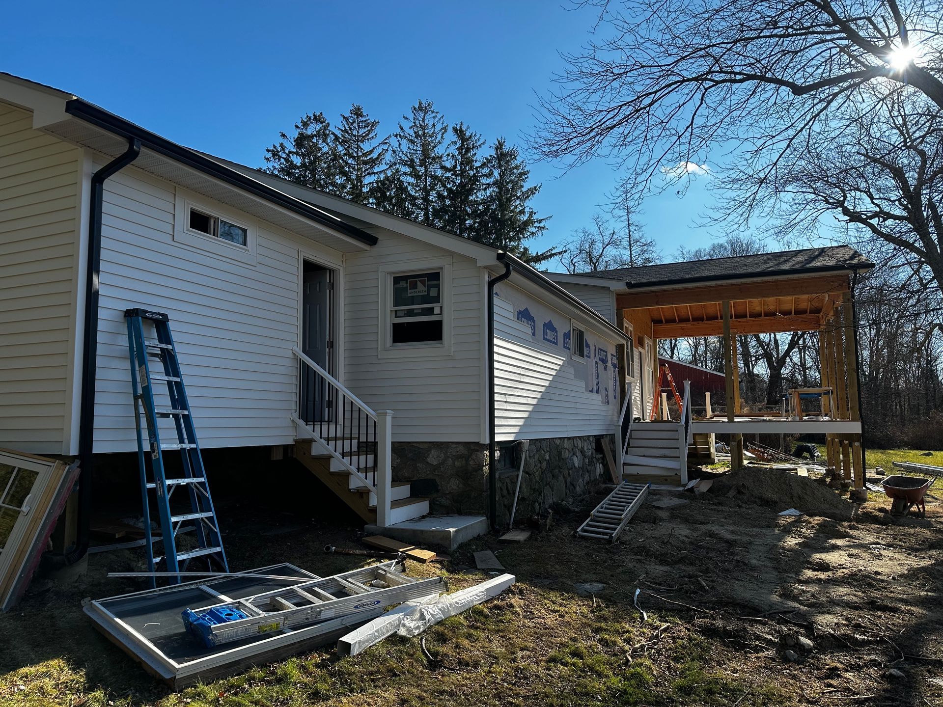 House under construction with white siding, blue ladder, and new porch.
