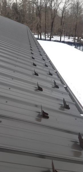 Metal roof with snow guards. Winter scene with trees in the background.