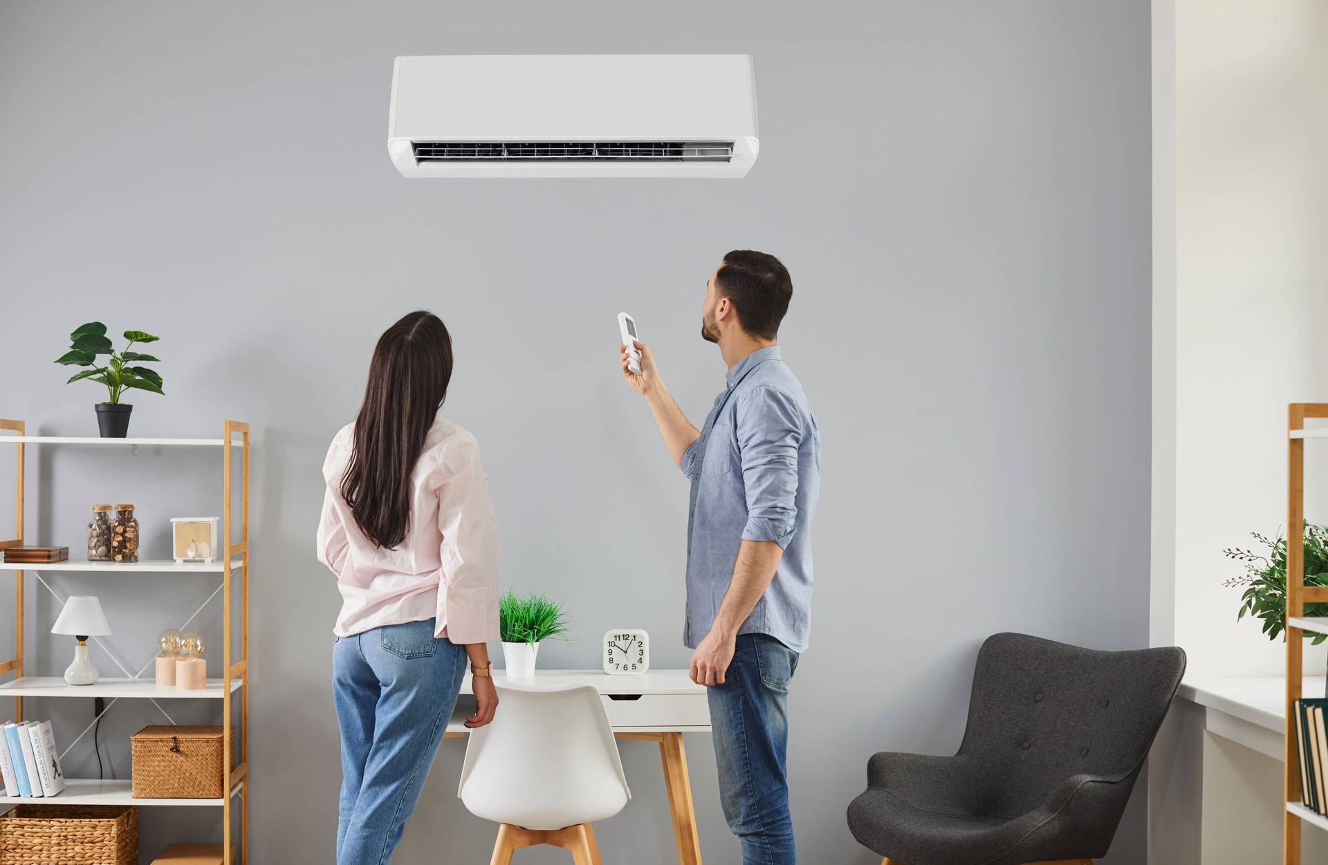 Two people in a living room use a smartphone to control a wall-mounted air conditioner.