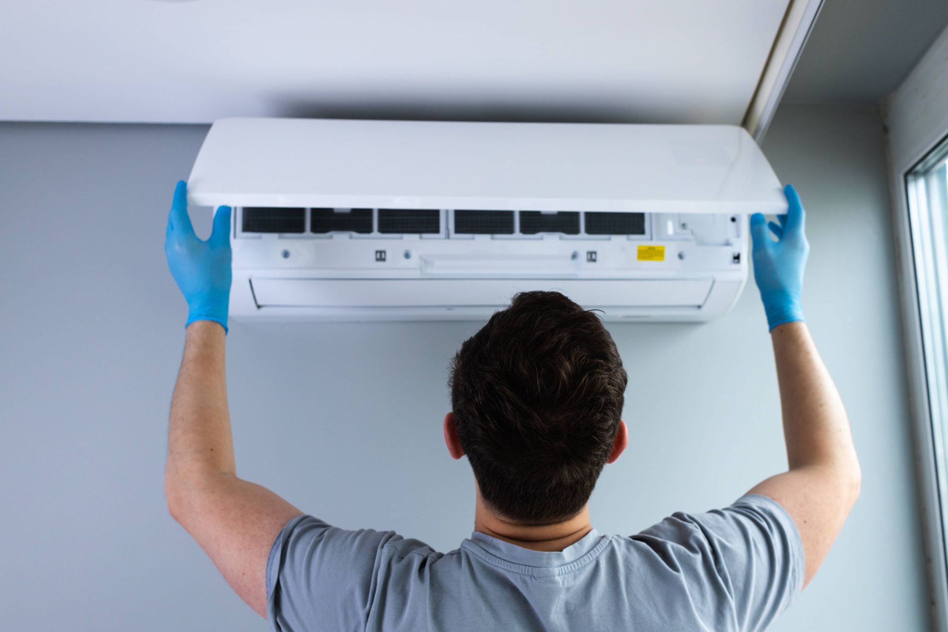 Technician in blue gloves installing a wall-mounted air conditioner indoors