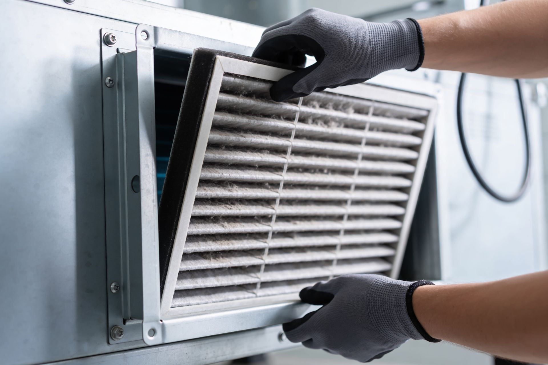 Gloved hands removing a dirty HVAC air filter from a metal vent panel