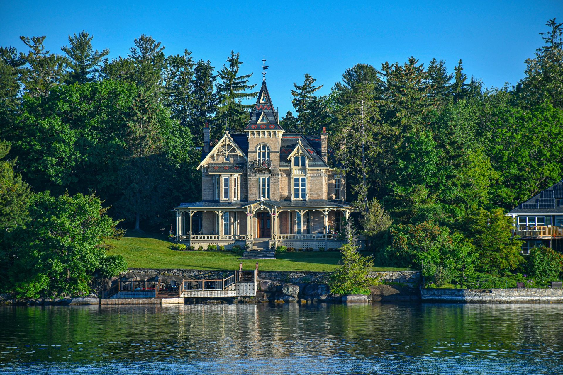 A large house sits on the shore of a lake surrounded by trees