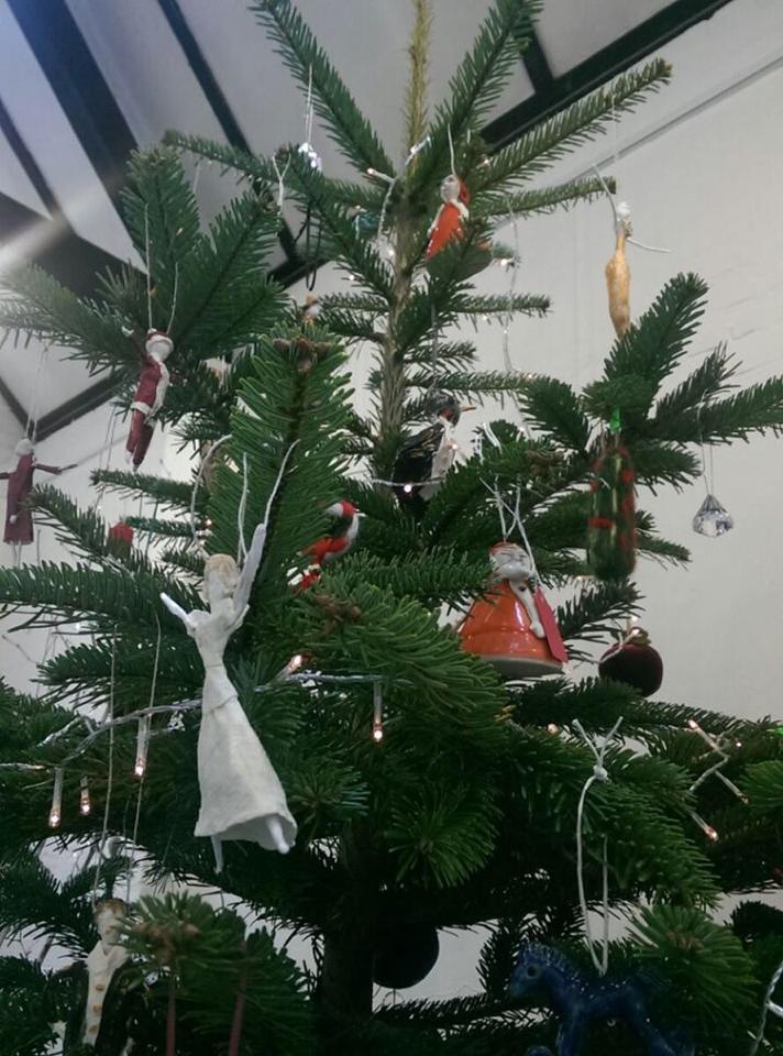 Christmas tree with ornaments and string lights against a white wall.