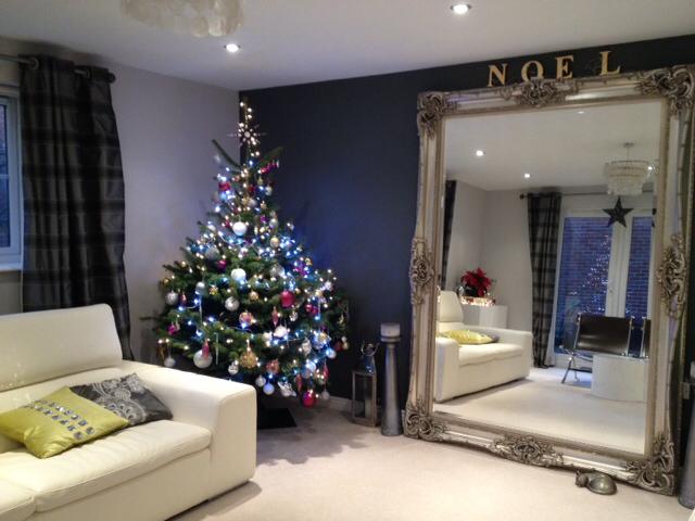 Christmas tree in a decorated living room with large ornate mirror and white sofa. 