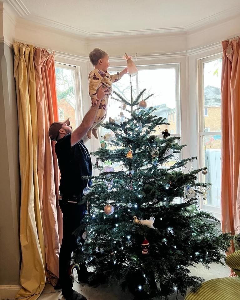 Man lifting child to place star on Christmas tree in brightly lit room.