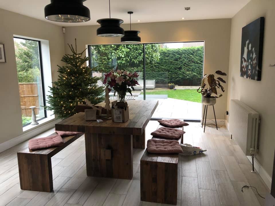 Dining room with large wooden table, benches, Christmas tree, and view of a garden.