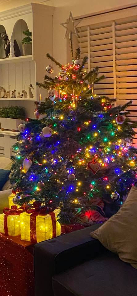 Christmas tree decorated with colorful lights and ornaments, beside a lit gift.