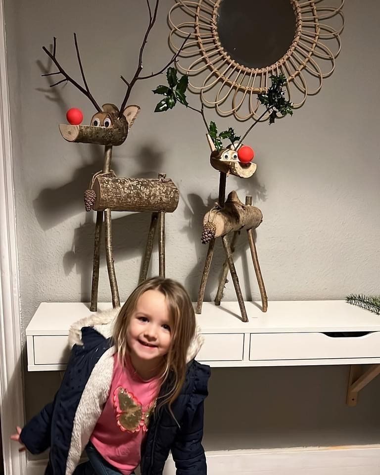 Girl smiles in front of a white console table with wooden reindeer decor and a circular woven mirror.