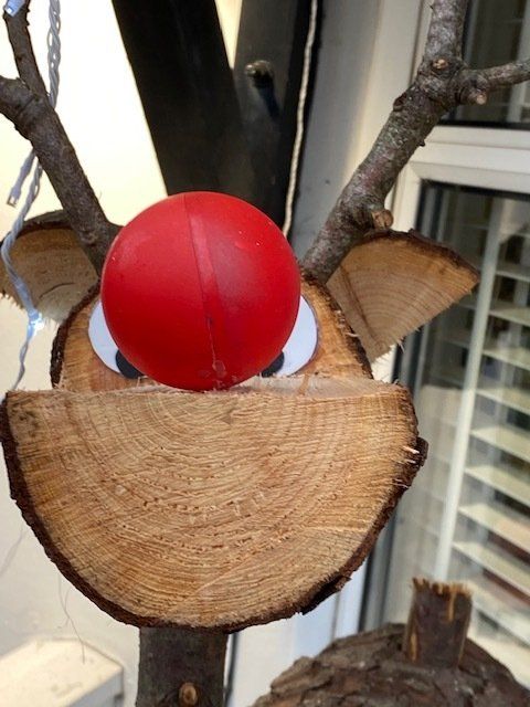 Rudolph the reindeer crafted from wood slices, with a red nose, twig antlers, and painted eyes.