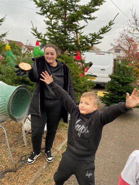 Woman holding disc, boy with arms outstretched, near Christmas trees outside.