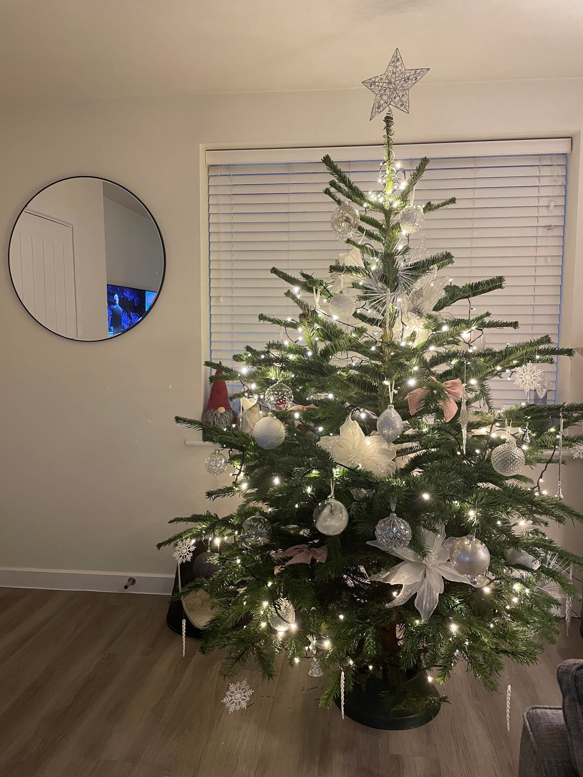 Christmas tree decorated with lights and ornaments. A mirror hangs on the wall.