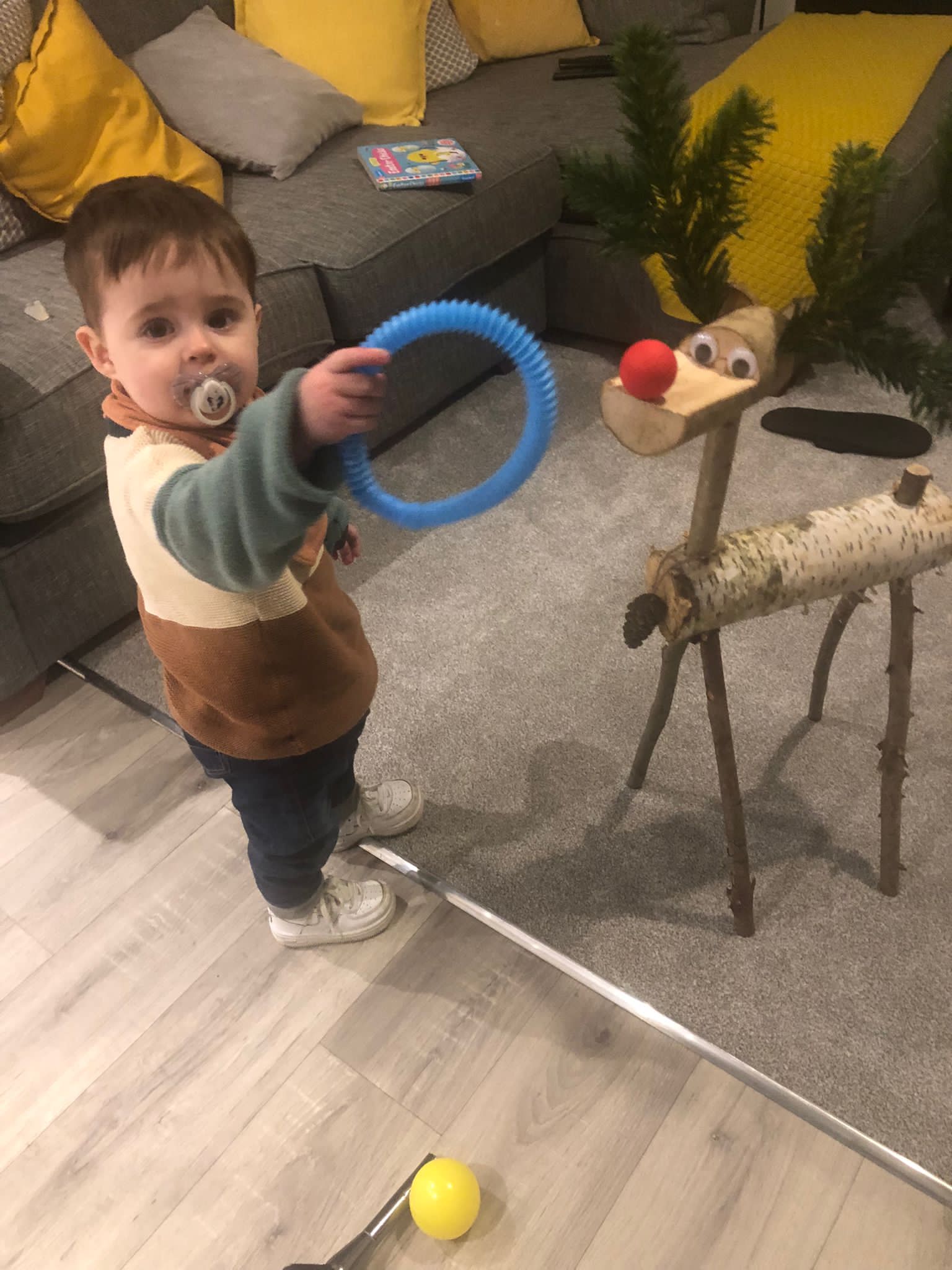 A child holding a blue ring, facing a wooden reindeer. Golf club and ball in foreground.