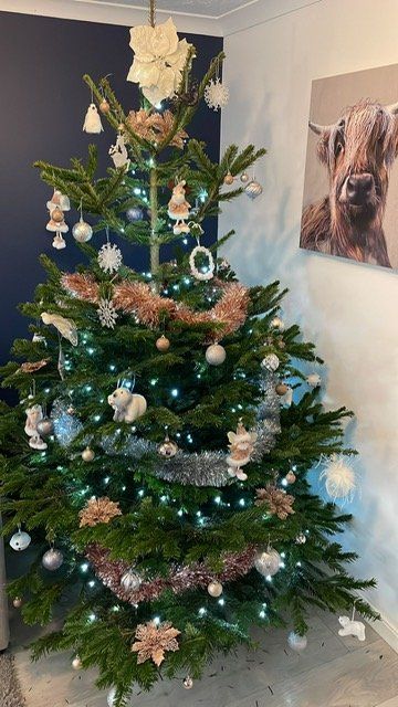 Christmas tree with lights, pink and silver ornaments, and garland. A Highland cow painting hangs on the wall.
