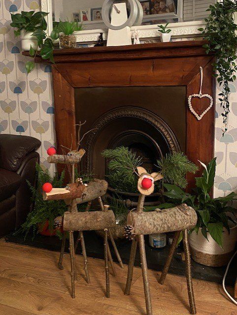 Three wooden reindeer decorations sit in front of a fireplace with greenery and a heart ornament.