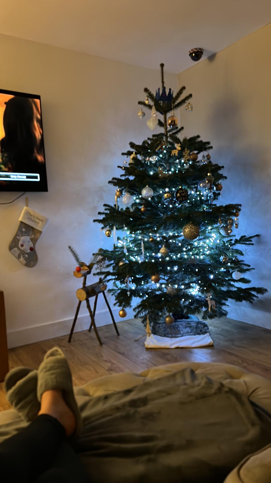 Christmas tree with white lights and ornaments in a living room, feet up in cozy slippers.