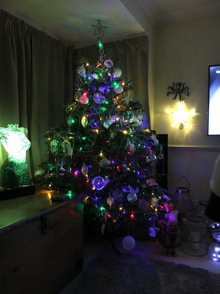 Christmas tree adorned with ornaments and lights in a room, with a star topper and colorful glow.
