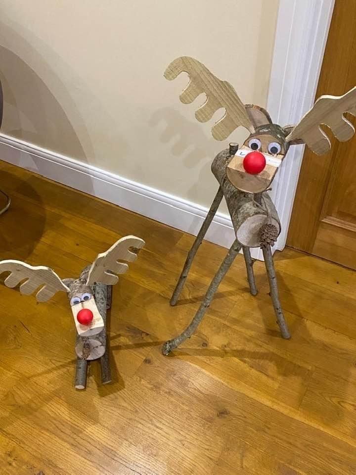 Two wooden reindeer decorations with twig bodies, wooden antlers, and red noses on a wood floor.
