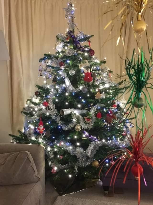 Christmas tree decorated with lights, ornaments, and tinsel in a living room.