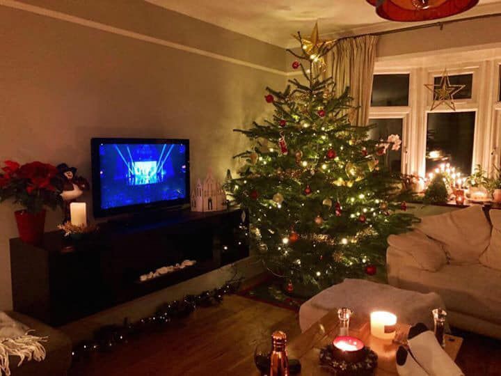 Cozy living room decorated for Christmas with a lit tree, TV, and candles.