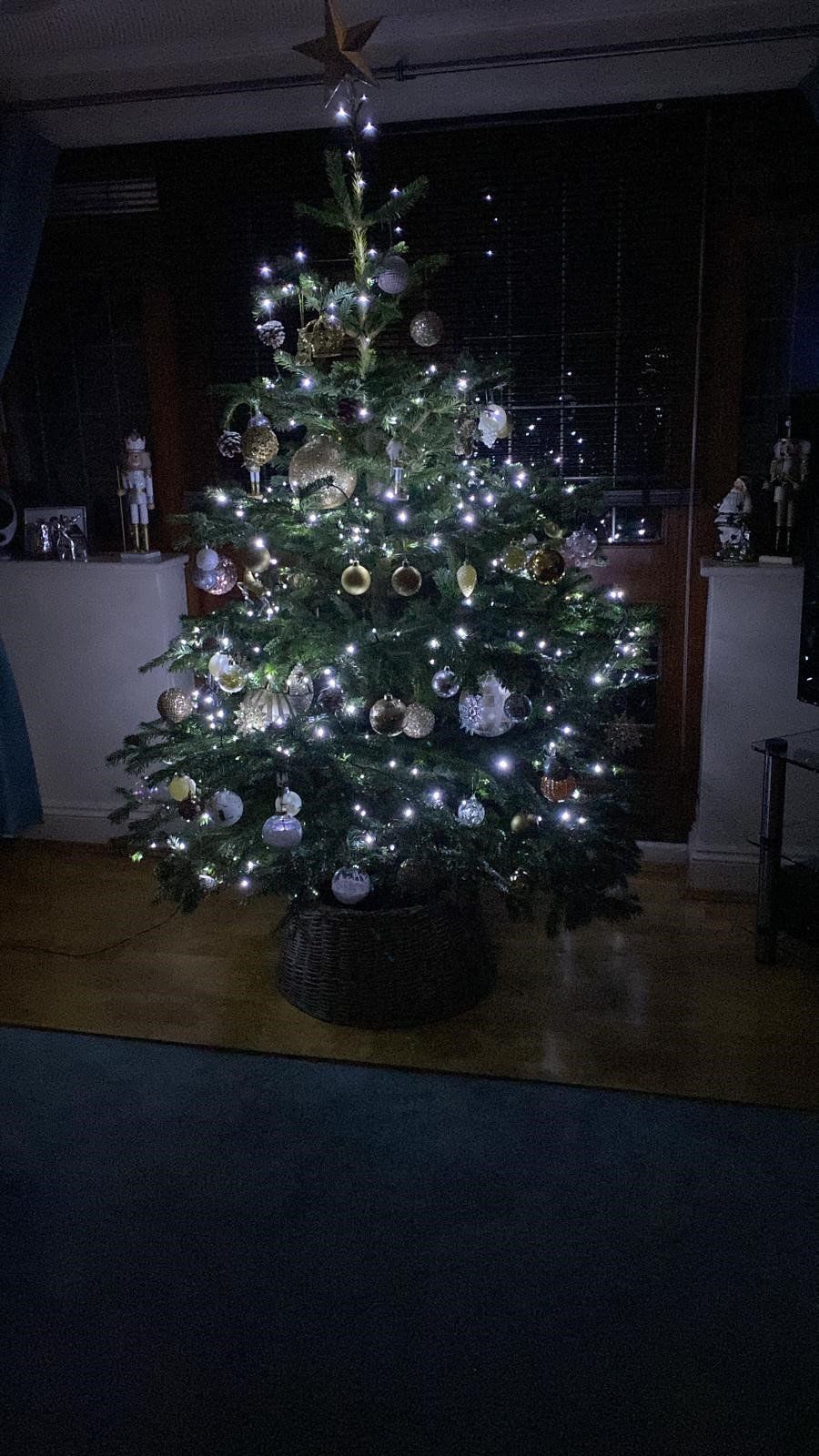 Lit Christmas tree with ornaments, star topper, in a dimly lit room.