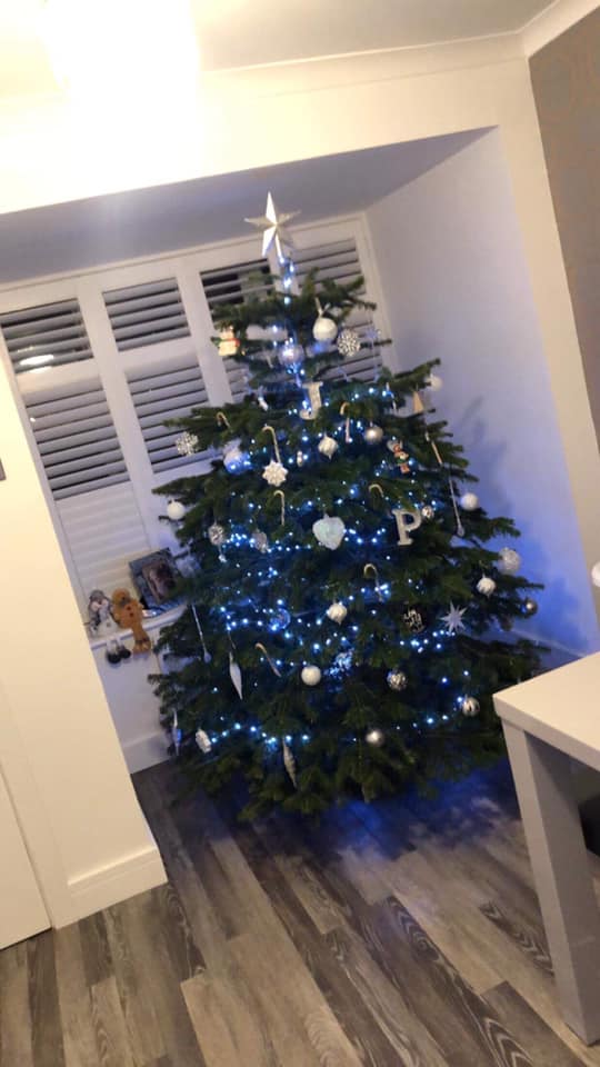 Christmas tree decorated with white ornaments and blue lights, in a room with shutters.