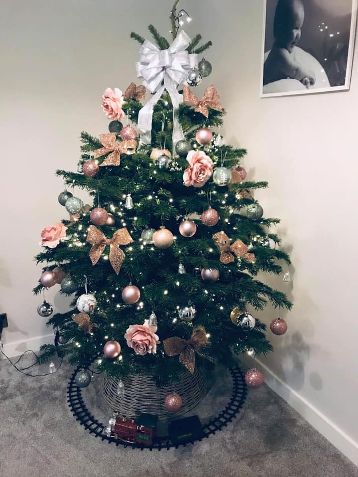 Christmas tree decorated with pink and silver ornaments, bows, and lights, train set base.