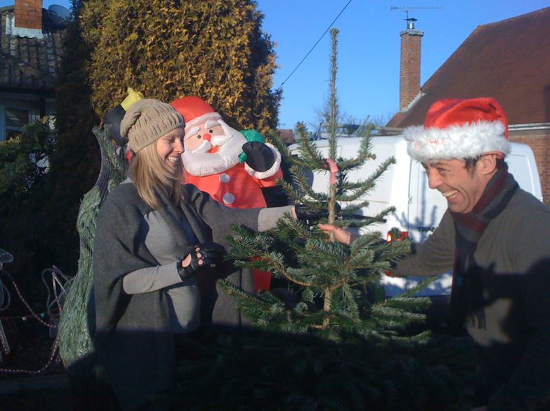 Couple selecting a Christmas tree with Santa Claus decoration in the background on a sunny day.