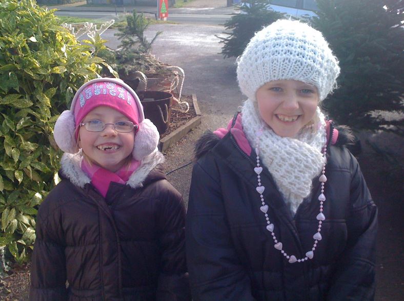 Two girls in winter coats and hats smile outdoors.