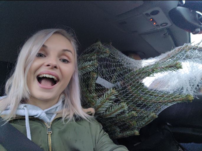 Woman in car with Christmas tree, smiling excitedly.