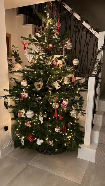 Christmas tree decorated with lights and ornaments near a staircase.