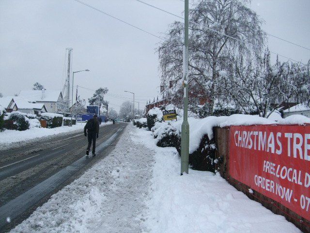 Snowy street scene. Person walks on snow-covered sidewalk; red 