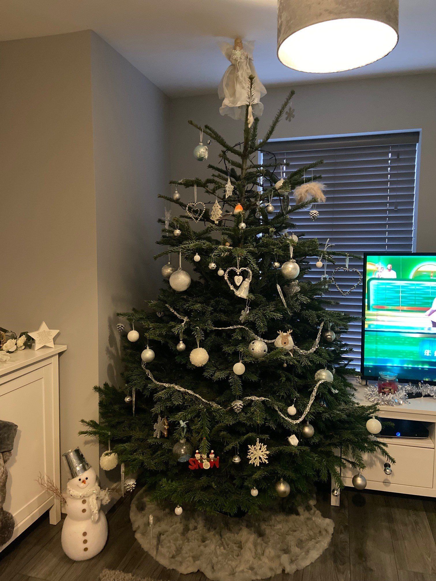 Christmas tree decorated with silver ornaments and a fuzzy tree skirt.