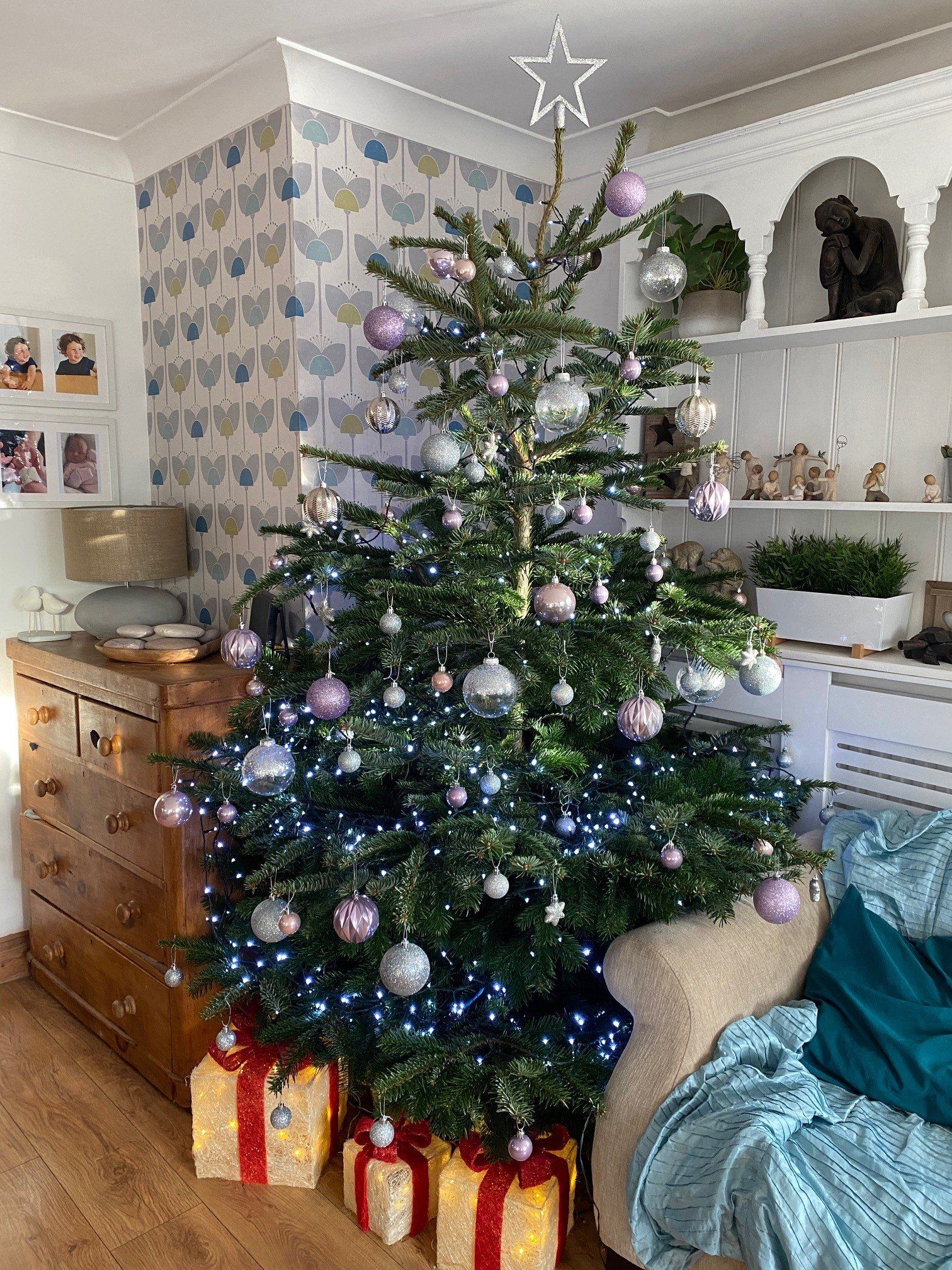 Christmas tree decorated with pink and silver ornaments, surrounded by presents, in a cozy living room.