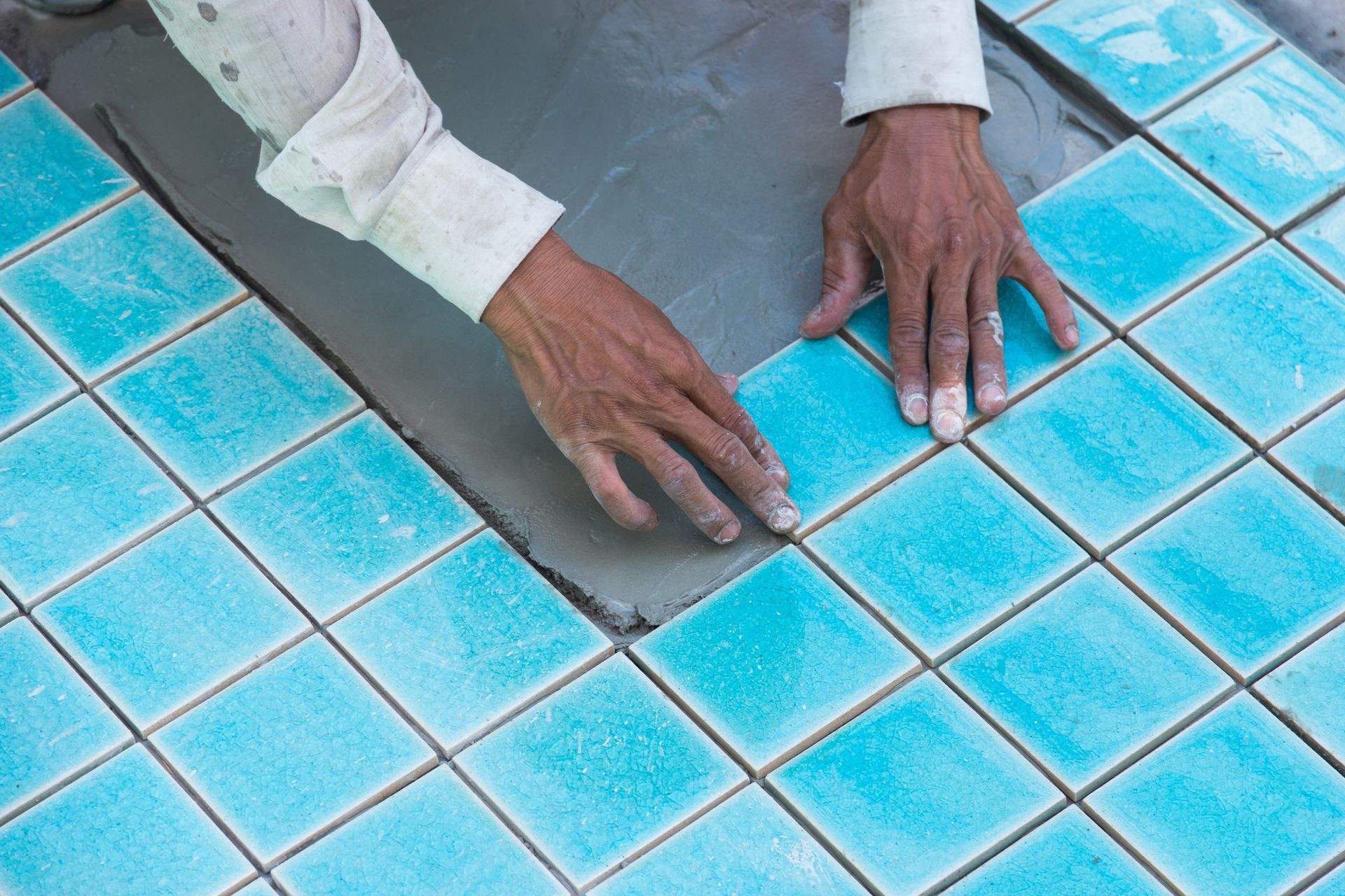 A builder installing tiles on a swimming pool. A builder installing tiles on a swimming pool.