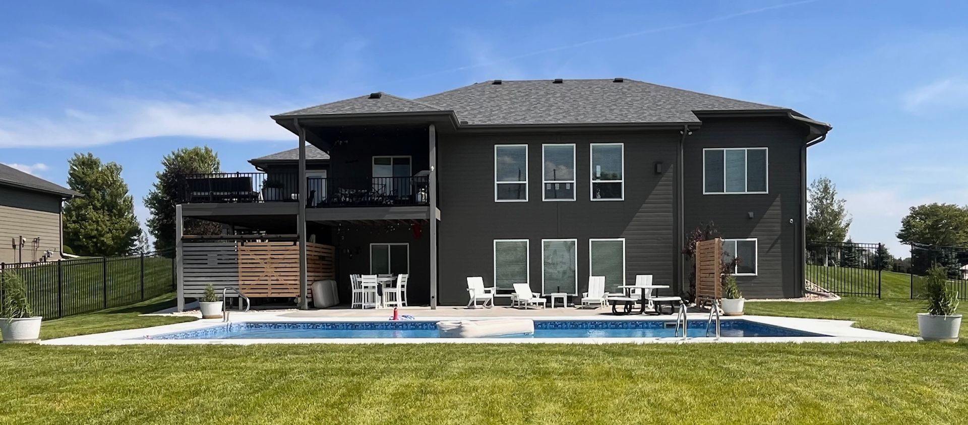 Back of a modern two-story gray house with pool and lawn on a sunny day.
