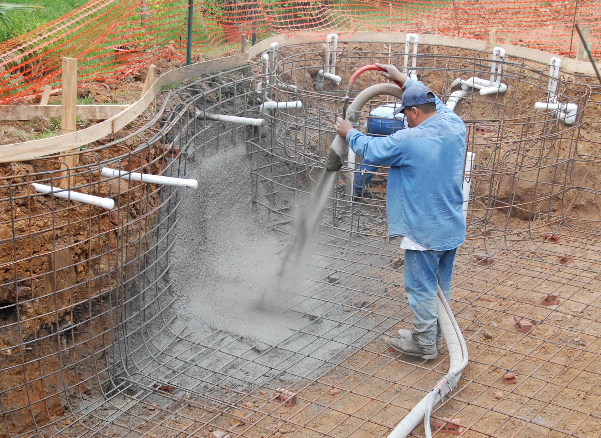 A builder sprays concrete to build a pool.