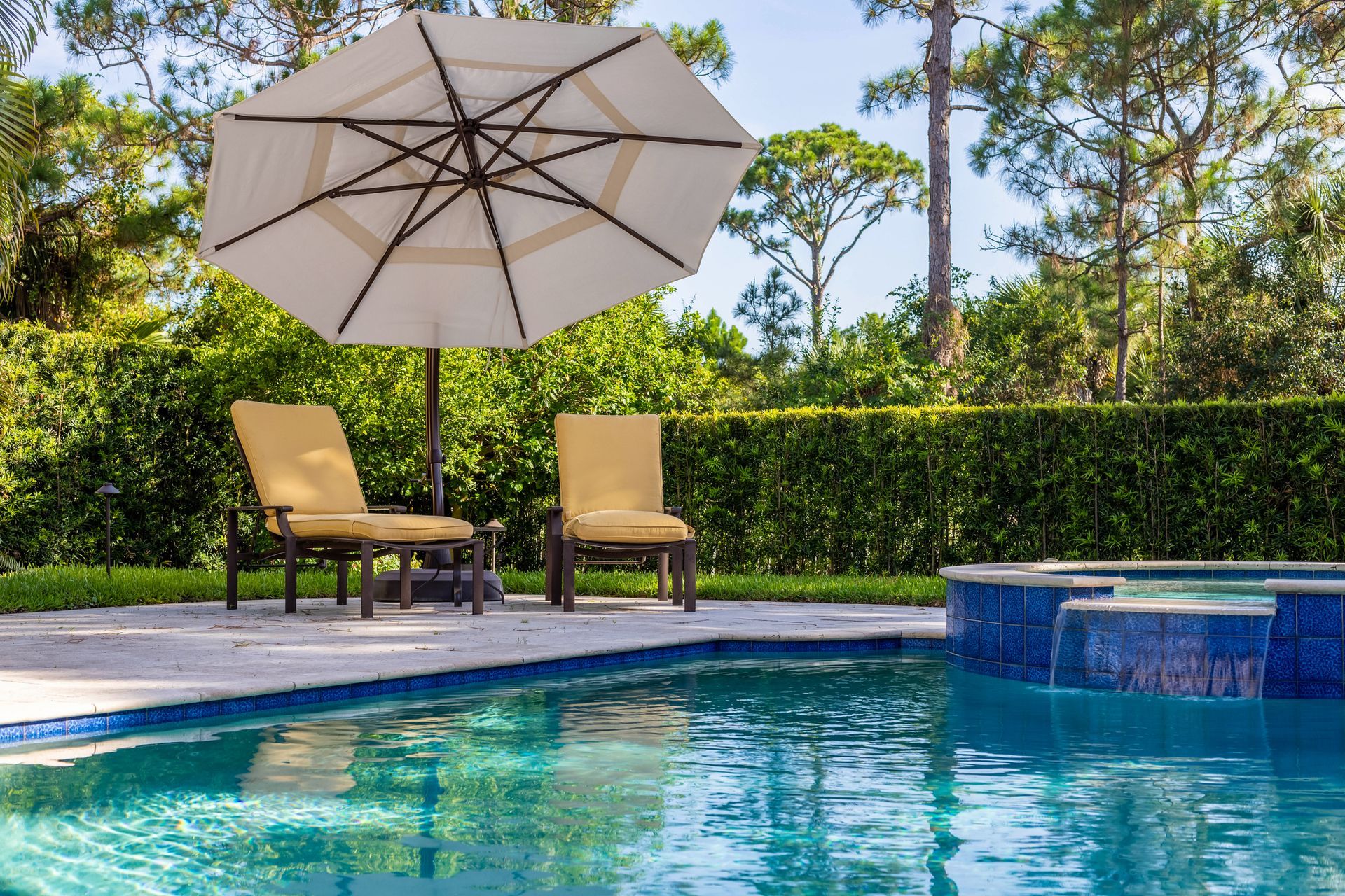 View of yellow sun loungers with an umbrella, and a pool with a spa, constructed by pool builders.