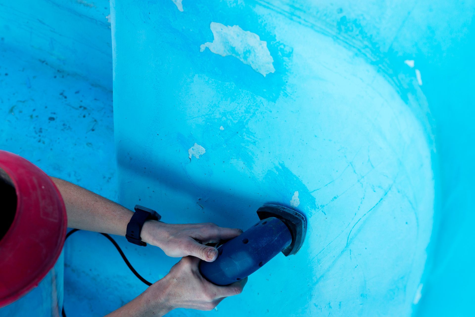 Woman in protective mask using sander on a pool wall, showcasing swimming pool renovation services.