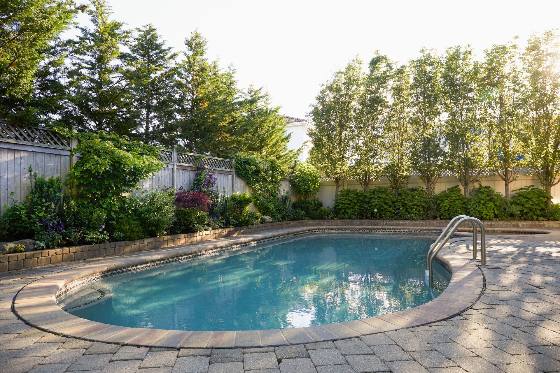 Backyard pool with stone patio, surrounded by trees and plants.