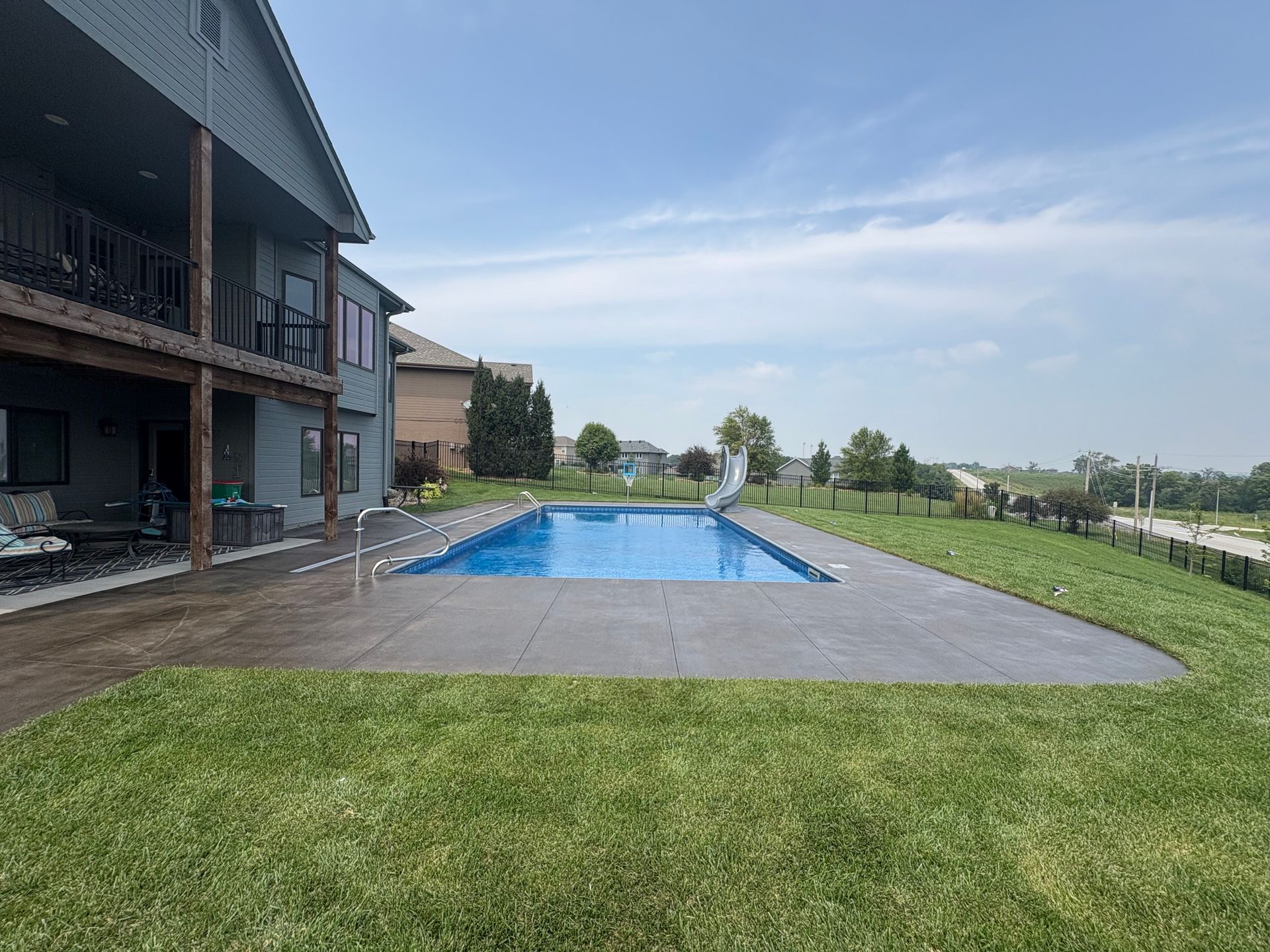 A backyard with a rectangular pool and a two-story house with a deck.