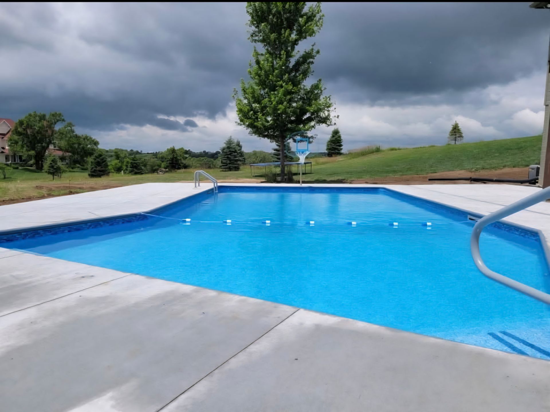 Rectangular swimming pool with blue water, concrete deck, and cloudy sky.