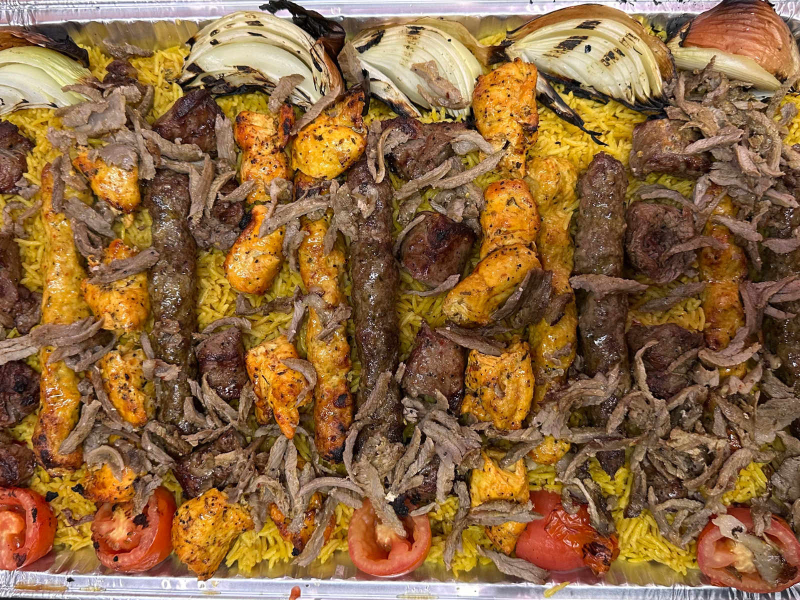 A large tray of yellow rice topped with grilled meats, onions, and tomatoes.