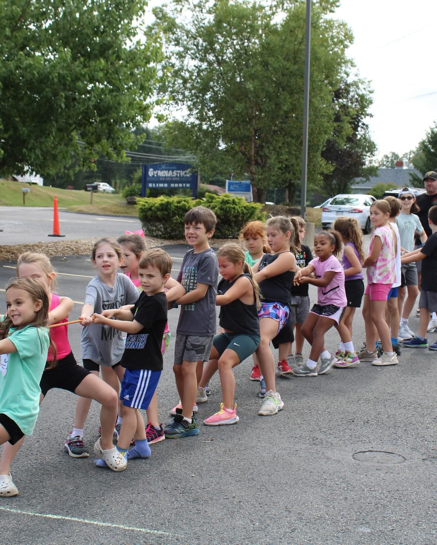 Children playing tug-of-war outdoors, pulling a rope. Green, black, and pink clothing.