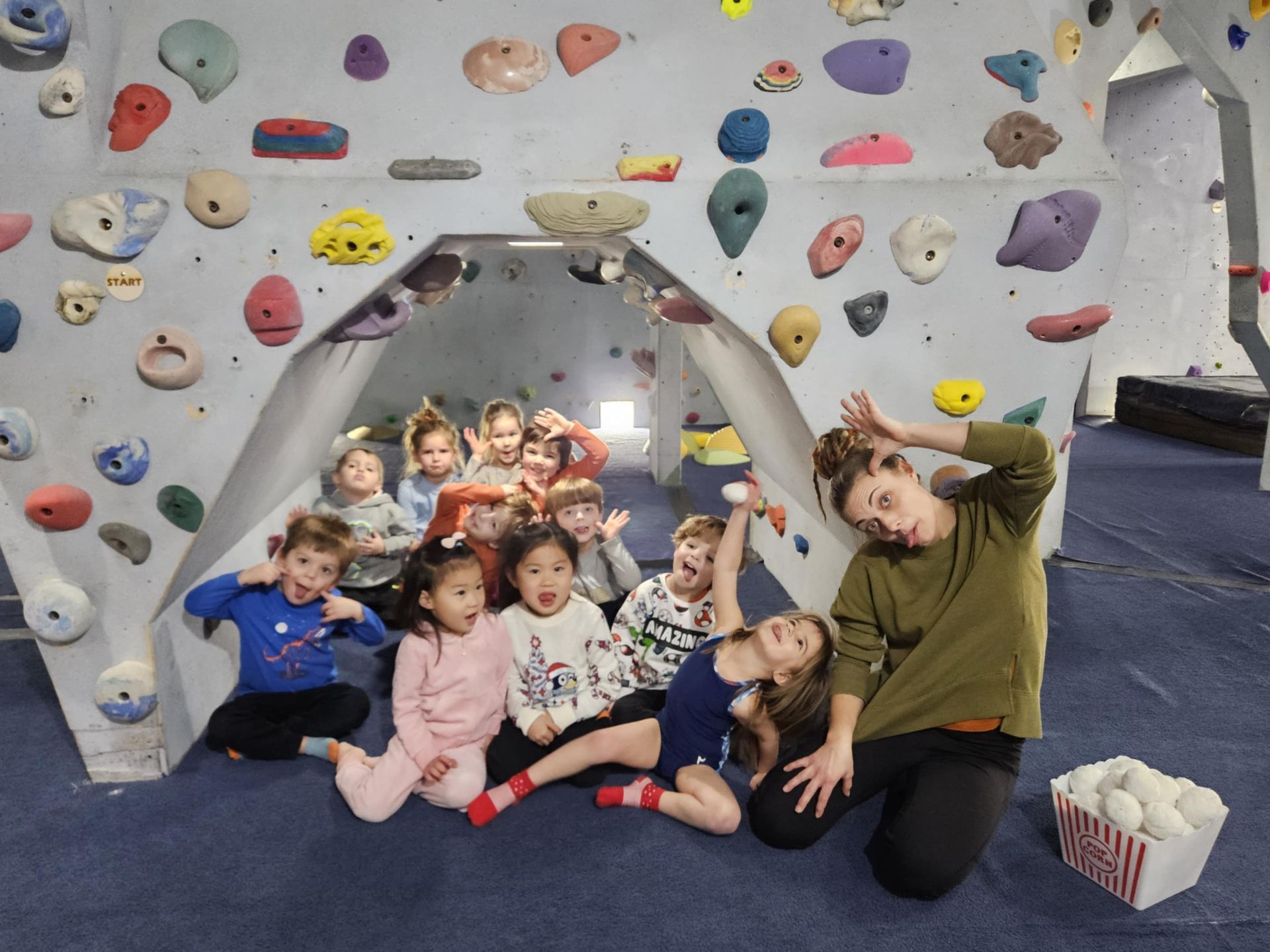 Group of children posing with instructor at a rock climbing gym. Smiling and making funny faces.