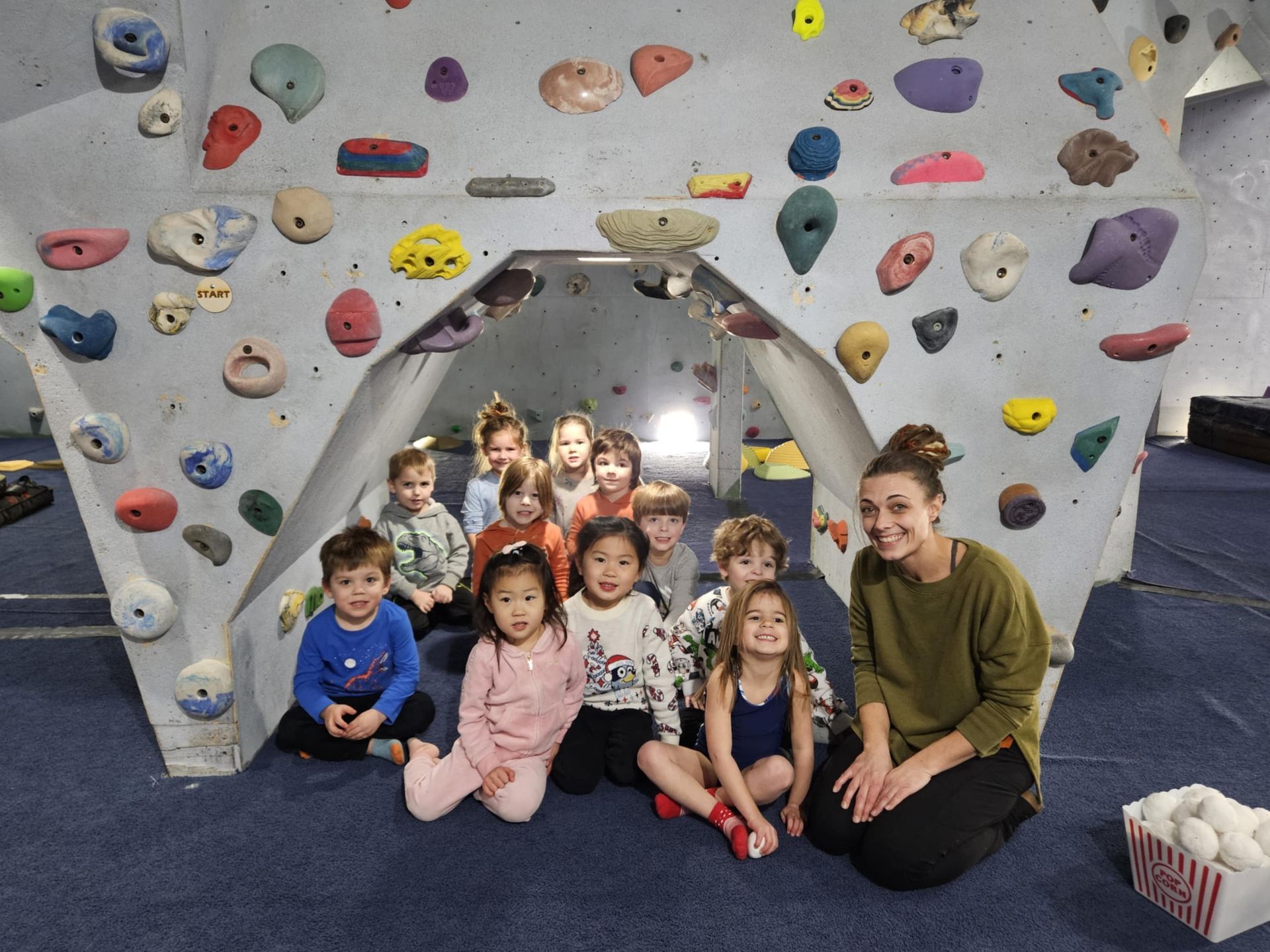 Children and instructor posing at a climbing wall, looking toward the camera.