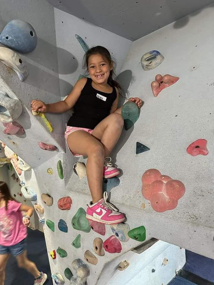 Young girl smiling, climbing a colorful indoor rock wall.